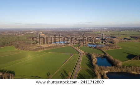 This aerial image captures the expansive beauty of the countryside, characterized by lush green fields that stretch into the distance, suggesting fertile agricultural land. A series of small lakes or
