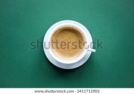 Cup of coffee close-up on a green background.  Delicate, tasty, aromatic cappuccino in a white cup on a white saucer, space for copy text, flat lay, top view.