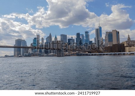 Stunning view of Manhattan skyscrapers from the Hudson River against a backdrop of blue sky with drifting white clouds on a sunny summer day.
