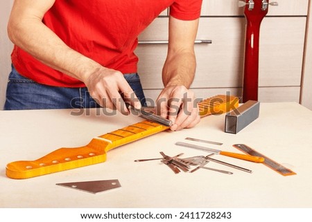 Guitar repairer crowning frets on the guitar neck with special fret files. Royalty-Free Stock Photo #2411728243