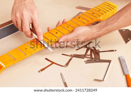Guitar repairman crowning frets on the guitar neck with special fret files. Royalty-Free Stock Photo #2411728249