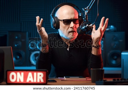 Professional expressive radio presenter working at the radio station, he is wearing headphones and talking into the microphone