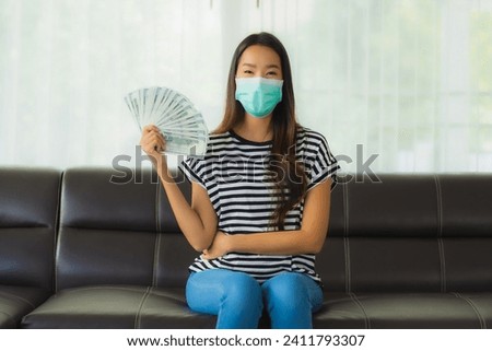 Portrait beautiful young asian woman with mask on sofa show money or cash at home Royalty-Free Stock Photo #2411793307