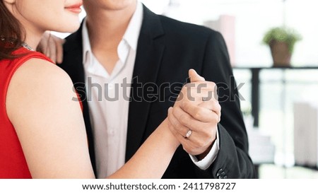 Newlyweds enjoy about waltz dance together and wear red dress and black handsome tuxedo while smiling and holding hand with wedding couple ring diamond fashion in Happy Anniversary Day Royalty-Free Stock Photo #2411798727