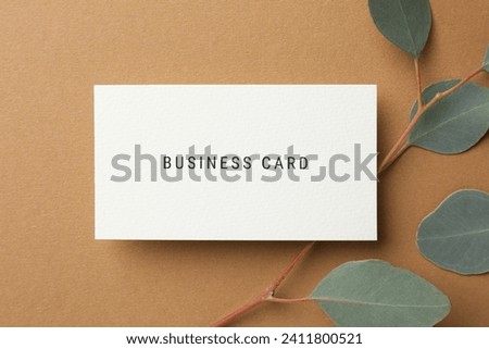Business card and eucalyptus branch on light brown background, top view