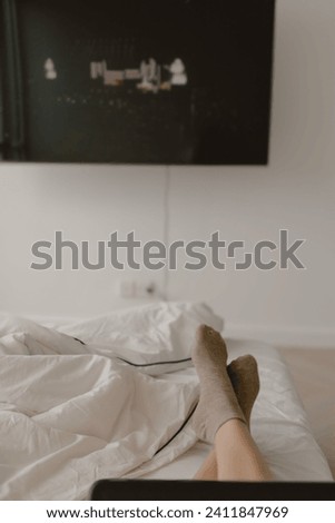 Image of woman legs feet, she using laptop for working at room home as freelance, showing black empty screen display, watching tv series, sitting on white bed alone. 