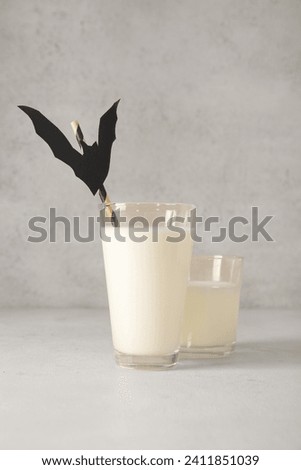 Glasses of milk and bat made of paper for Halloween on light background