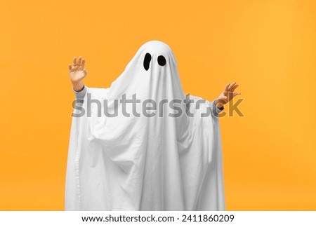 Child in white ghost costume on orange background. Halloween celebration