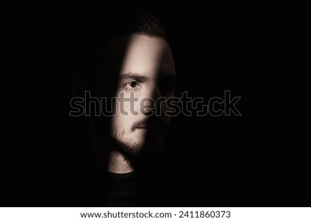 A man stands in the dark and a beam of light illuminates part of his face. Black background. Art photography. Psychological picture.