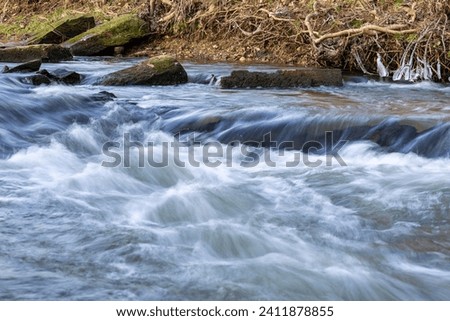 Water flowing quickly through a rapid of river Eschbach in Germany with waves, drops and splashes. Longtime exposure with motion Royalty-Free Stock Photo #2411878855