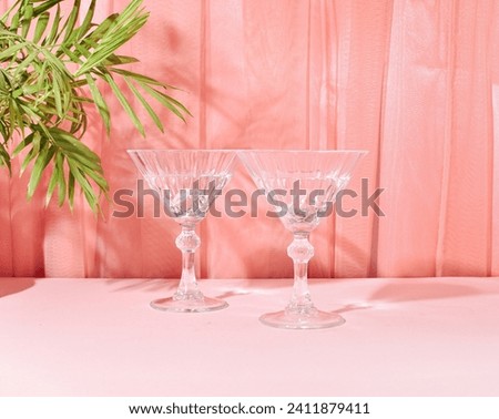 Two glasses of refreshing cocktails in the shade of a palm branch, pastel pink peach tulle curtain background, summer holiday romantic relax layout.