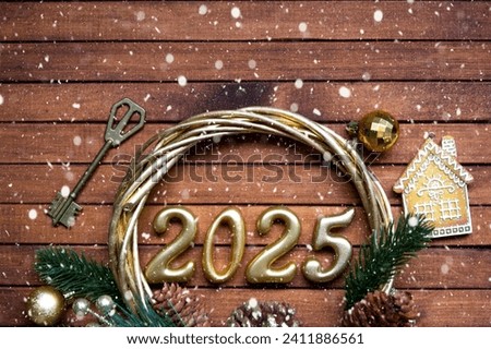New Year House key with keychain cottage on festive brown wooden background with number 2025 in wreath, lights of garlands. Purchase, construction, relocation, mortgage, insurance