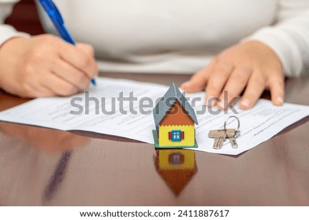 The client officially signs the document, the beginning of the real estate venture. There is a miniature house on the table, the joyful opening of a new house.