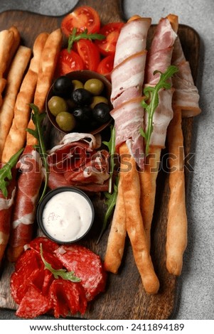 Wooden board of tasty Italian Grissini with bacon on light background Royalty-Free Stock Photo #2411894189