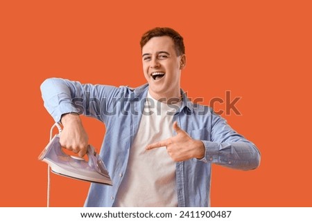 Handsome young man pointing at modern electric iron on orange background
