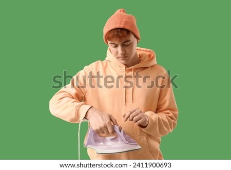 Handsome young man with electric iron on green background