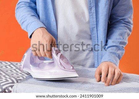 Man ironing shirt on orange background, closeup