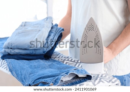 Man with electric iron and stack of clean clothes on board, closeup