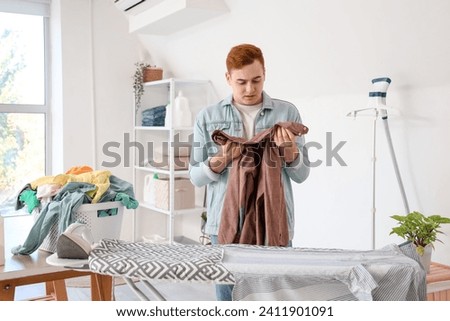 Young man sorting clothes near ironing board in laundry room