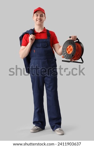 Male electrician with extension cord reel on light background Royalty-Free Stock Photo #2411903637