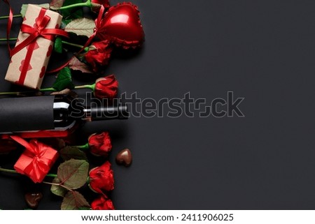 Bottle of wine with gift boxes, chocolate candies, heart shaped air balloon and red roses on black background. Valentine's Day celebration