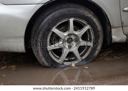 Deflated car wheel. Punctured tire. Wheel in a puddle. The car in detail. Royalty-Free Stock Photo #2411912789