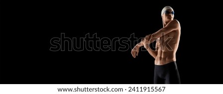 Muscular, athletic young man, swimmer in goggles and cap stretching muscular body before swim over black background.. Banner. Empty space to insert text. Concept of water sport events Royalty-Free Stock Photo #2411915567