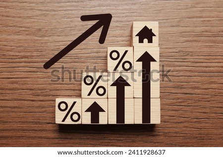 Mortgage rate rising illustrated by upward arrows, cubes with percent signs and house icon on wooden background, flat lay