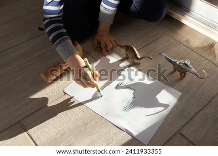 child draws contrasting shadows from toy dinosaurs on paper. ideas for children's creativity. Interesting activities for children at home and in kindergarten. View from above. little scientist