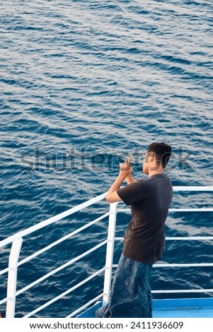 A man standing on the deck of the ship taking pictures. man taking picture of beautiful sunset over sea