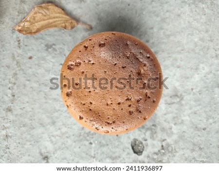 A nearly burnt and somewhat brown cupcake and a dry leaf from a fallen tree served as decorations for the photo session on the gray cement floor.taking picture of food in sunny day with natural light.