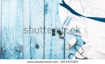 Sewing accessories. Clothes designer work desk. scissors, thread, white textile, satin or silk fabric on blue wooden background