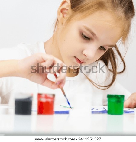 a little child girl paints a drawing with a brush in an album and smiles, a happy child draws a gouache picture at home at the table.