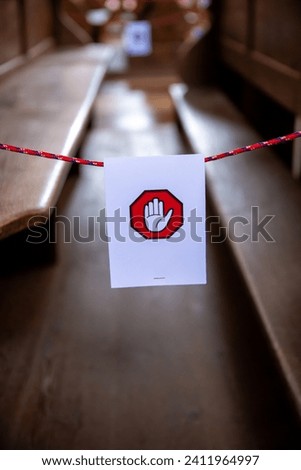 A white sign hung on a string with a symbol of a hand on a red hexagon. The sign is intended to indicate that the pews behind it cannot be used.