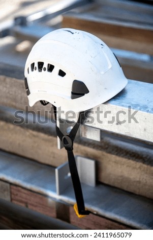 A white safety helmet placed on a metal carrier. The ventilation holes and the chin straps are clearly visible. Royalty-Free Stock Photo #2411965079