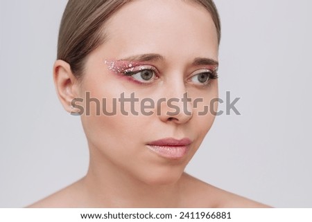 Young caucasian woman with purple and pink eye shadow and glitter on the eyelids on a gray background. Festive makeup. Party, holiday makeover