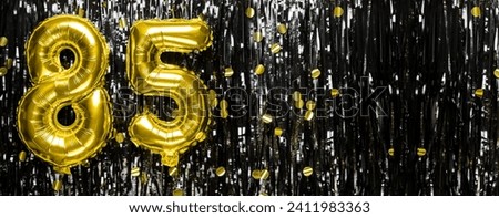 Gold foil balloon number number 85 on a background of black tinsel decoration. Birthday greeting card, inscription eighty-five. Anniversary event. Banner. copy space.