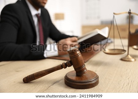 Lawyer reading book at table in office, focus on gavel