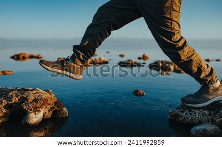 Boy walking on stones in the lake close-up view Royalty-Free Stock Photo #2411992859