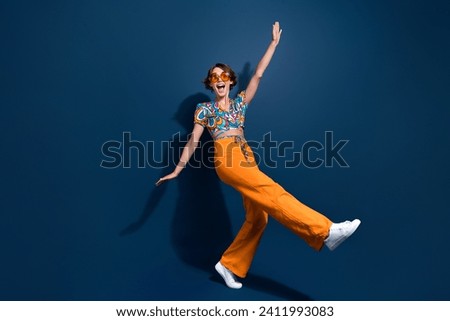 Full length photo of lovely young lady raise hands dancing have fun wear trendy flared pants isolated on dark blue color background