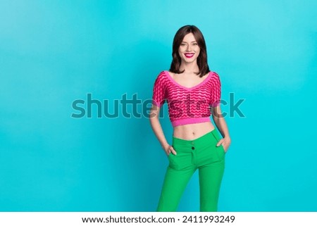 Portrait of toothy beaming optimistic woman with stylish hairdo wear pink top hold arms in pockets isolated on blue color background