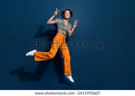 Full length photo of lovely young lady running showing double v-sign wear trendy flared pants isolated on dark blue color background