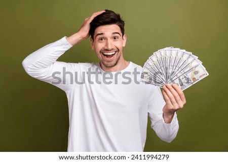 Photo of young business man in white pullover holding banknotes when realizes that he has become rich isolated on khaki color background