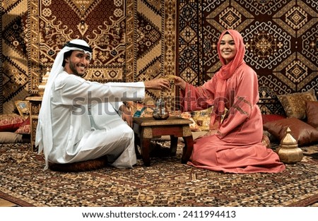 Young couple from Emirati spending time in an arabian traditional cafe. Man and woman wearing kandura and abaya from Dubai conversating together.