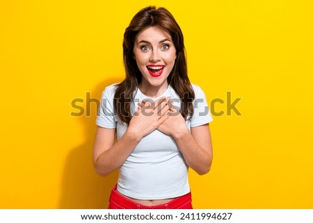 Photo of overjoyed ecstatic woman with brunette hair dressed white t-shirt hold hands on chest staring isolated on yellow color background
