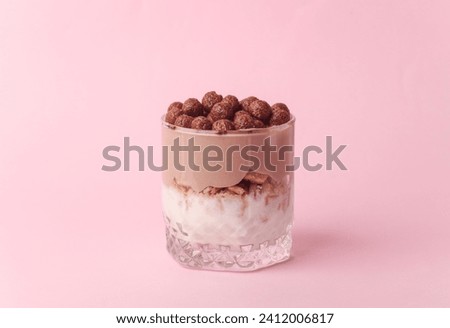 Homemade layered Desserts in a glass cups with yogurt and chocolate balls on a pink background