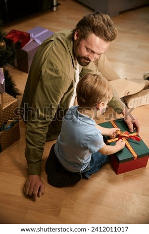 Man and little boy sit on floor opening Christmas present celebrating New Year