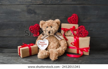Decorative card, on a wooden background on the table a teddy bear sits with gifts and red hearts on Valentine's Day.  Love theme concept.  Foreground, background image, front view.