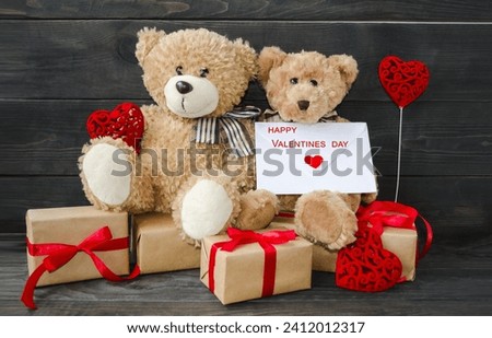 Decorative card, on a wooden background on the table sit teddy bears with gifts and red hearts on Valentine's day. Love theme concept. Foreground, background image, front view.


