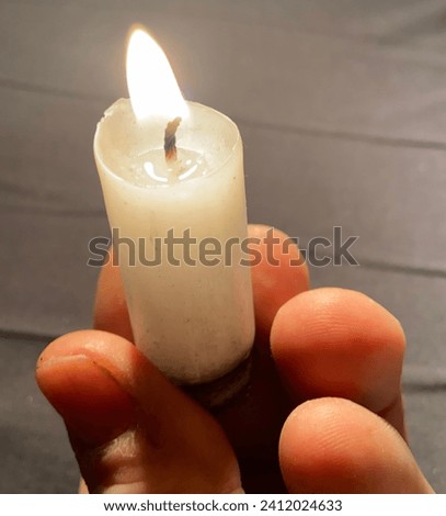 Small wax candle lit. Natural light from flame. Religious object from the Catholic church. Image with neutral and light background.